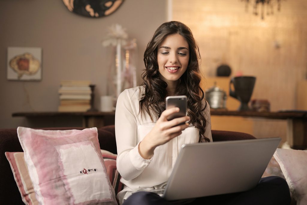 woman-sitting-on-sofa-while-looking-at-phone-with-laptop woman-sitting-on-sofa-while-looking-at-phone-with-laptop